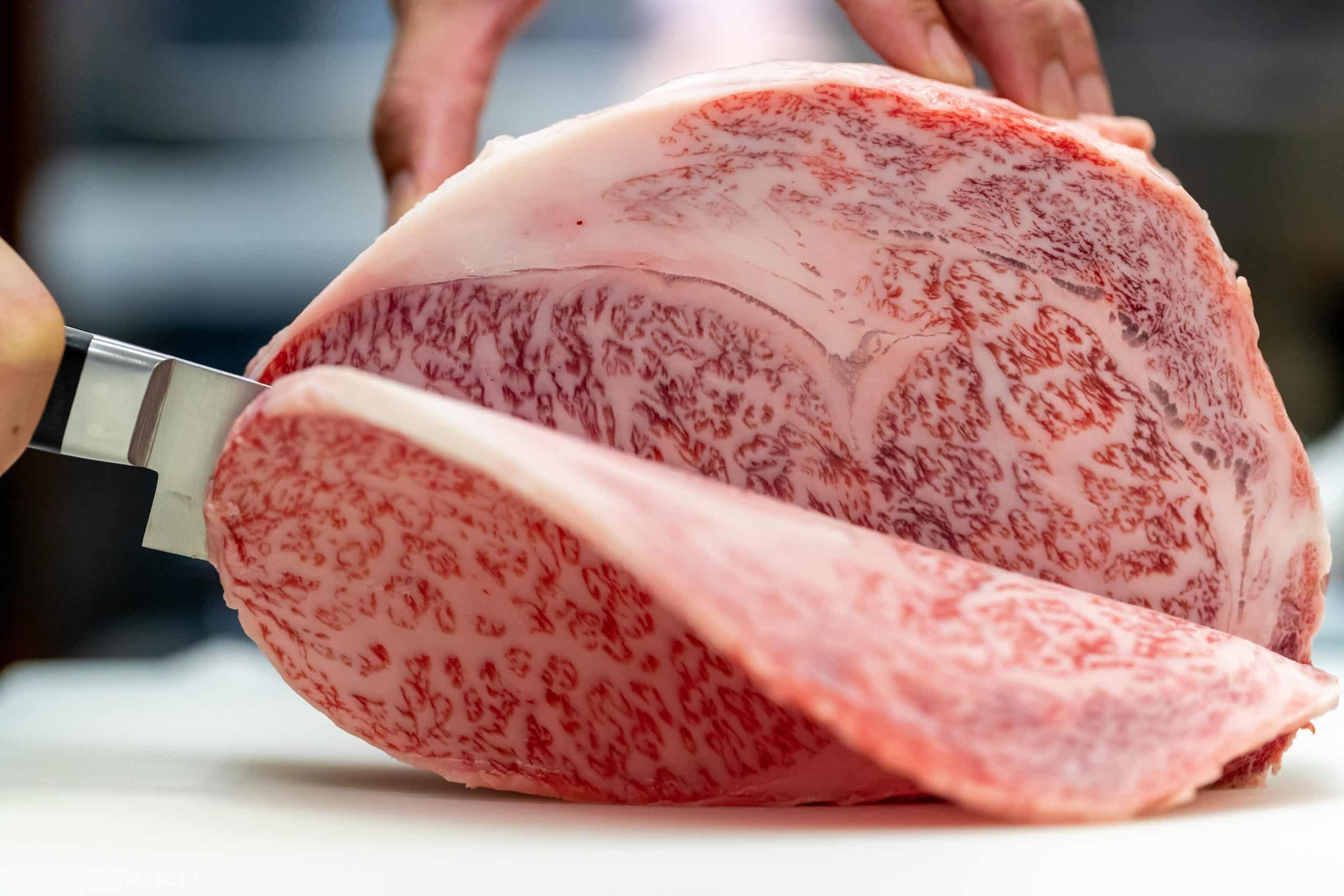 和食レストランの板前が厨房で最高級和牛の霜降り塊肉を丁寧に切り分ける職人技の調理シーン
